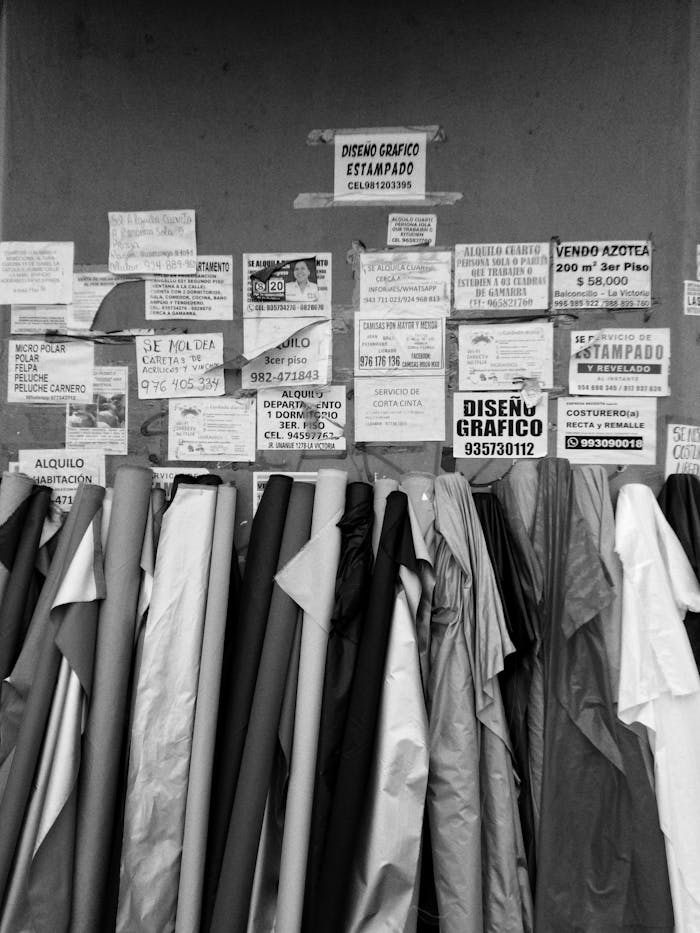 services-03 Black and white image of fabric rolls with various posters on a noticeboard in Perú.